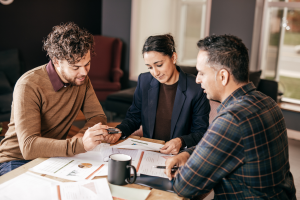 2 men and a women sitting down at a table with paper, discussing finance
